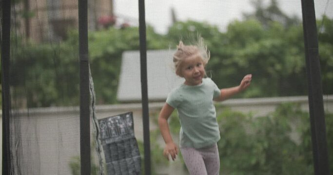 beautiful young girl jumping on a trampoline, trembling, being dynamic and playing outdoor in backyard on summer days