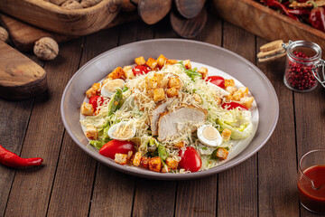 Plate of caesar salad with chicken and lettuce on wooden background