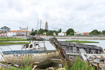 Fototapeta premium Noirmoutier en l'île, bateaux en bois échoué, Cimetière à bateaux, église Saint-Philbert et château en fond, île de Noirmoutier, Vendée