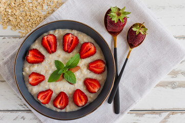 Homemade oatmeal with strawberries in bowl on white wooden background. Healthy breakfast. Top view.