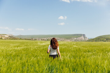 beautiful brunette woman walking through a field of wheat looks at the nature