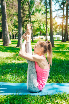 Sporty flexible woman doing yoga exercises in a city park outdoors. Vertical photography.