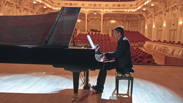 Pianist playing on a grand piano on big stage in concert hall