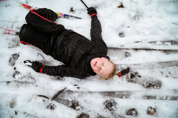 Caucasian boy lying in the snow after falling over while skiing