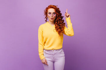 Redhead girl in glasses had idea. Woman in yellow sweater posing on lilac background