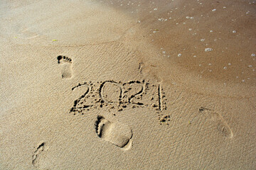 End of year 2021, lettering on the beach with sea wave. Numbers 2021 disappear on the seashore, message handwritten in the sand
