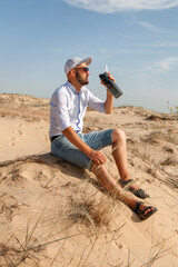 a man sitting on the sand in the desert holding a water bottle in his hand in the summer