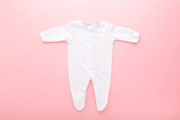 White new baby pajama with long arms and legs on light pink table background. Pastel color....