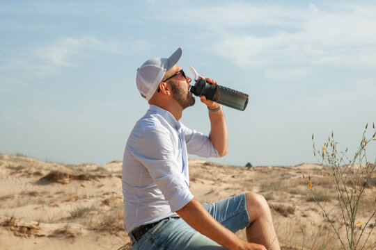 a man sitting on the sand in the desert holding a water bottle in his hand in the summer