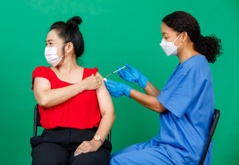 Asian female nurse in scrubs wearing mask holding syringe injecting Covid 19 vaccine to patient....