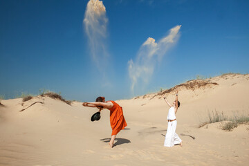 two women throw sand up in the desert in the summer