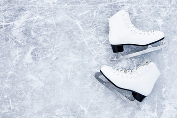 White female figure skates on ice background. Sport accessories for outdoor activities in cold winter season. Closeup. Empty place for text. Top down view.