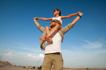 a man holds a child on his shoulders while in the desert in the summer