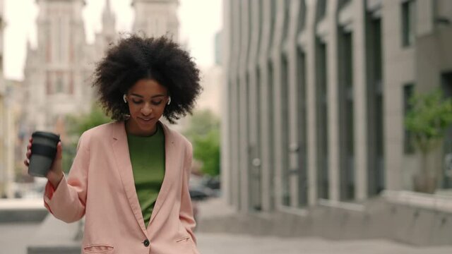 Smiling multiracial young business woman in formal outfit looking to camera outside on street and feeling happy while listening music. Business beautiful modern manager concept.
