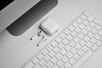 Close-up of Keyboard computer, wireless earphones on white office desk. White wireless earphones...