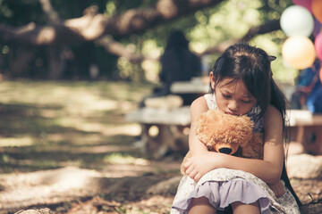 Sad girl hugging teddy bear sadness alone in green garden park. Lonely girl feeling sad unhappy...