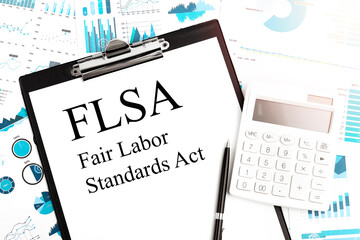 Text FLSA - Fair Labor Standards Act on clipboard, pen, calculator, charts. Business concept. Flat lay.