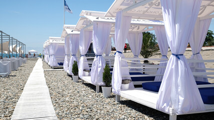 White beach canopies with white curtains. Summer luxury bungalows on beach resort. Luxury area for relaxing on the beach Black Sea in Sochi, Russia.