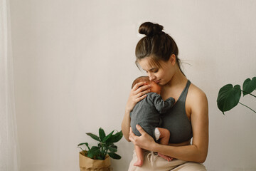 Mother holds and hugs her newborn baby son at home. Happy infant and mom.