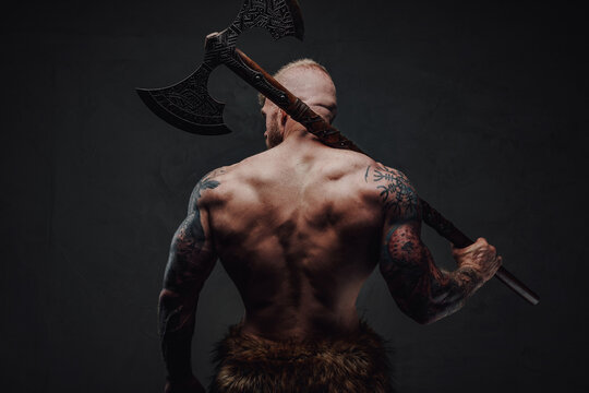 Rear view of healthy tattoed warrior in fur with axe on a dark background