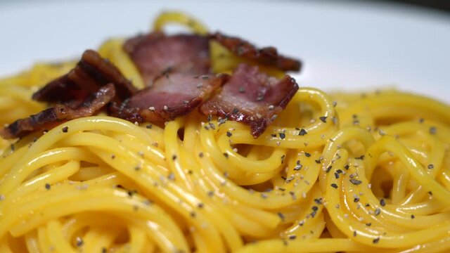 Spaghetti carbonara, a traditional pasta dish of Italian culture made with fresh egg yolk, original grated pecorino romano, crispy bacon, and black pepper.