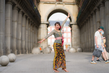young happy and beautiful Asian woman wearing traditional Balinese kebaya dress - Indonesian girl doing Bali dance on street during holidays travel in Europe