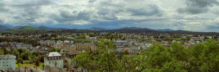 Fototapeta na wymiar Vista panorámica de la ciudad de Oloron-Sainte-Marie en un nublado día de junio, Francia. Los tejados de los edificios y las verdes colinas al fondo.