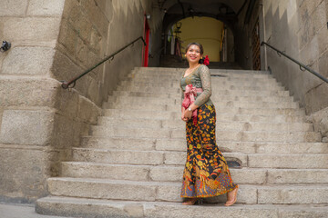 Fototapeta na wymiar young happy and beautiful Asian woman wearing traditional Balinese kebaya dress - Indonesian girl in Bali clothes walking on street during holidays travel in Europe
