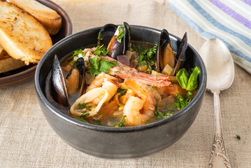 Soup with seafood, shrimps, squid rings and mussels on a plate on a table with toast