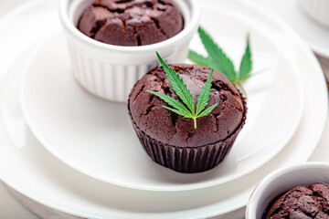 Marijuana chocolate cupcake muffins with weed cbd. Medical marijuana hemp drugs in food dessert. Weed muffins with cannabis and cannabis leaves served on white plate