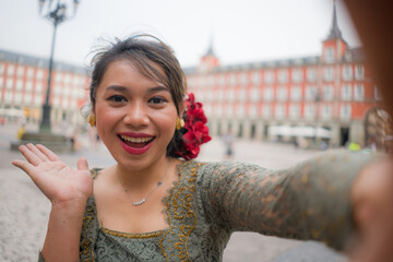 young happy and beautiful Asian woman wearing traditional Balinese kebaya dress taking selfie - Indonesian girl in Bali clothes walking on city street during holidays in Europe