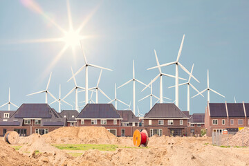 Construction site of new Dutch family homes with large wind turbines and sun in the background
