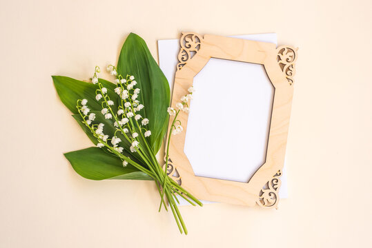 Small bouquet of lilies of the valley wooden frame and blank card with space for design on beige background view from above