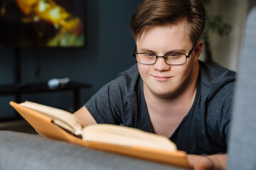 Young man with down syndrome reading book while lying on couch