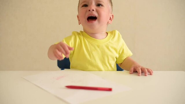 toddler boy plays draws on a piece of paper with a red pen sitting at a white table. educational game Montessori fine motor skills. early development concept