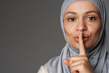 Middle eastern woman in hijab showing silence gesture at camera