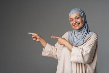 Middle eastern woman in hijab smiling and pointing fingers aside