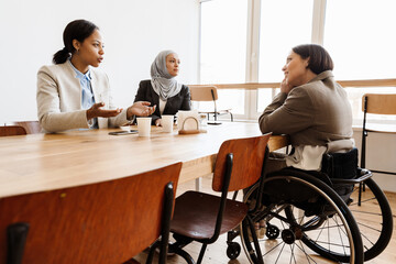 Three multiracial women discussing project while having break in office