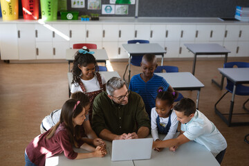Caucasian male teacher and group of diverse students using laptop together in the class at school