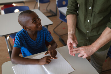 Mid section of male teacher talking in hand sign language with african american boy at school