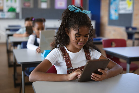 African american girl using digital tablet while sitting on her desk in the class at school
