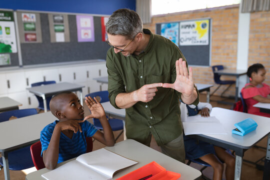 Caucasian male teacher and african american boy talking in hand sign language at school