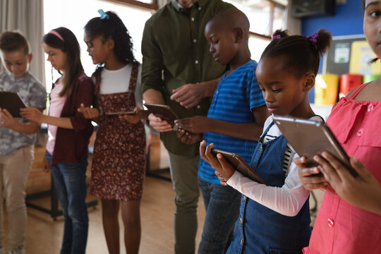 Caucasian male teacher and group of diverse students using digital tablets in the class at school