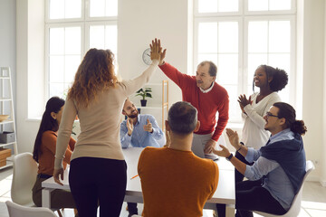 Happy young and mature coworkers and teammates high fiving each other in office meeting. Diverse business colleagues and partners celebrating successful deal. Teamwork, success and diversity concept