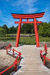 View of a red Japanese gate with a pond covered with water lilies in the background 