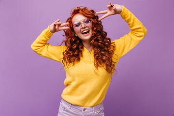 Portrait of naughty girl in lilac glasses and cashmere sweater. Teen shows signs of peace on...