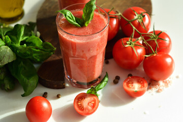 Two glasses of fresh organic tomato juice decorated with raw tomatoes and green leaves of basil on...