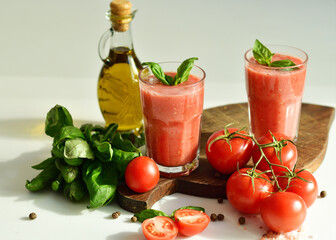 Two glasses of fresh organic tomato juice decorated with raw tomatoes and green leaves of basil on light background.Healthy diet nutrition concept.
