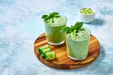 Cucumber Gazpacho - cold summer soup with basil in glasses on wooden board on light background