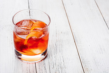 Glass with dark orange beverage. Lemon rind and ice. Negroni with bitter and vermouth.